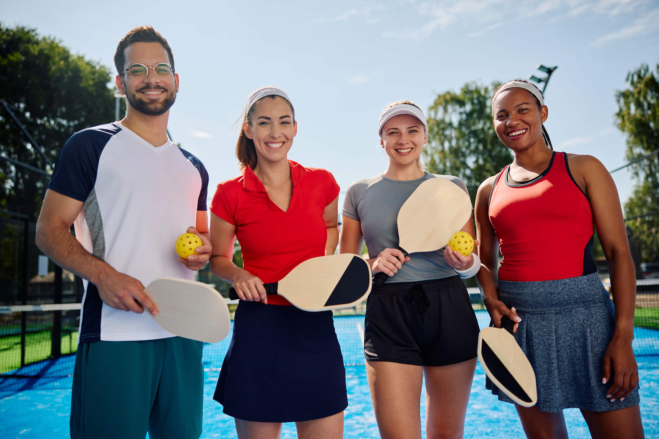 Four vibrant, happy pickleball players holding paddles