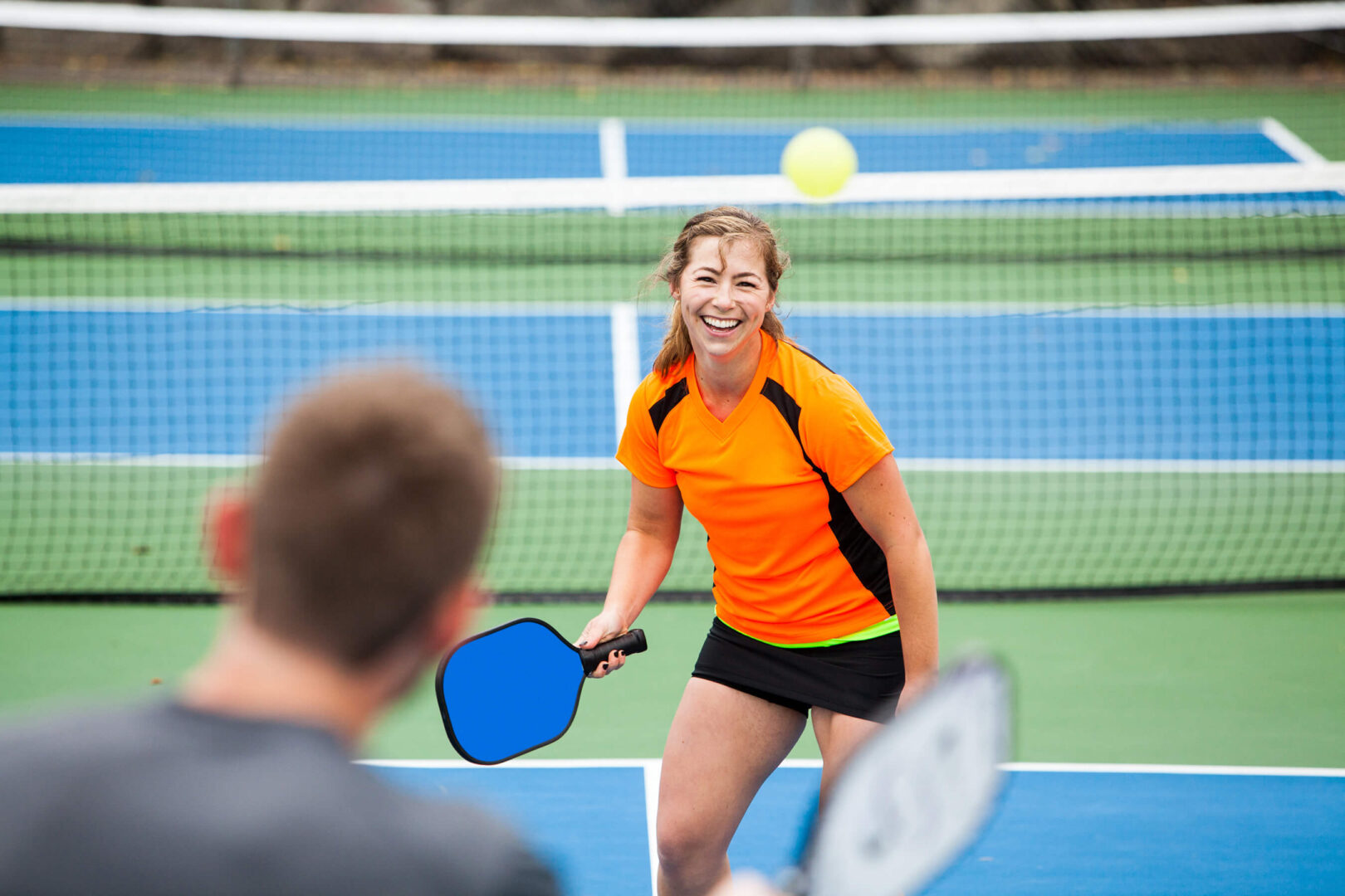 Smiling female pickleball players at the net returning a ball